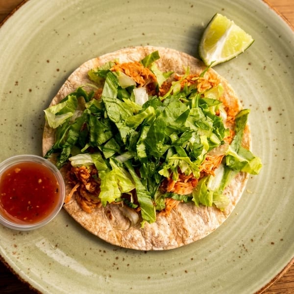 A chicken taco with lettuce, a side of salsa, and a lime wedge on a green plate.