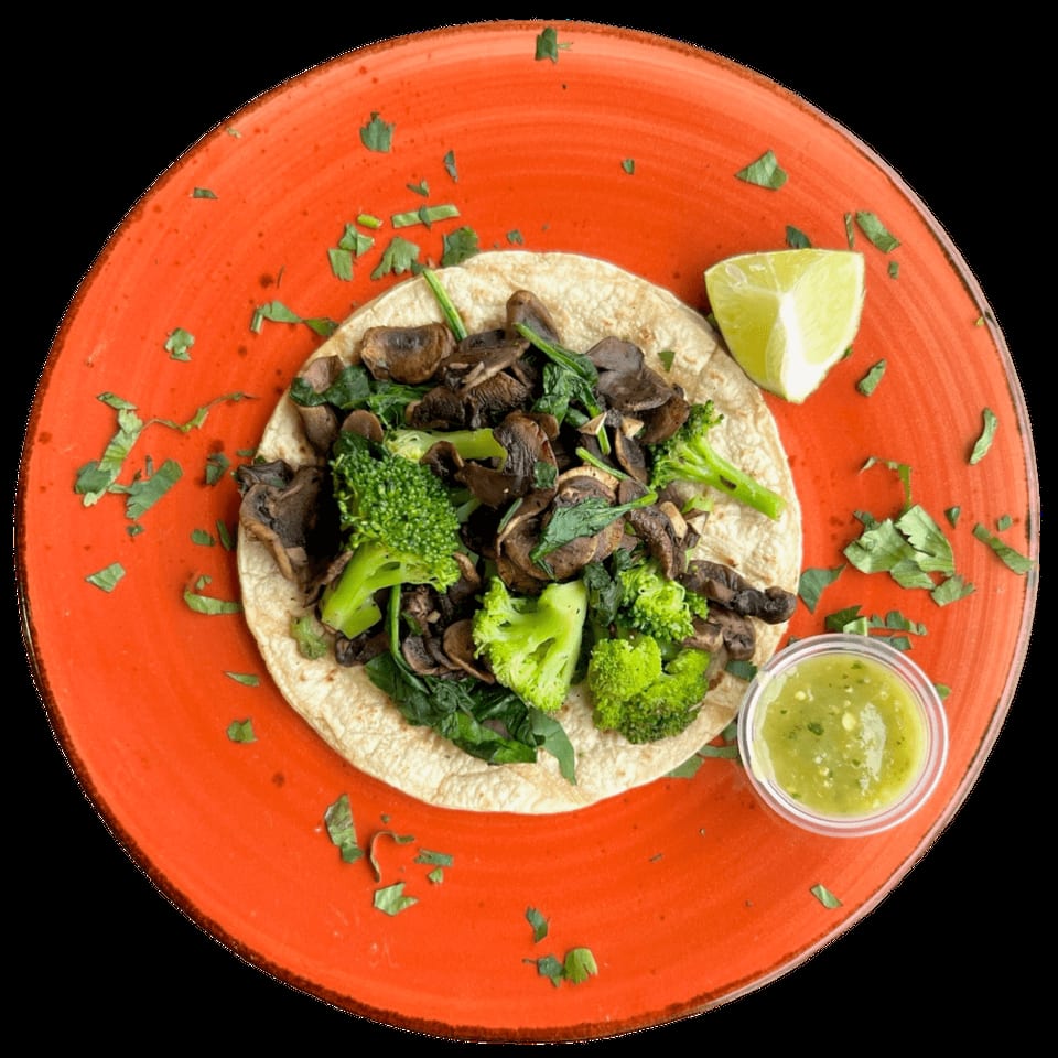 Vegetable taco with mushrooms, broccoli, and spinach, served with salsa verde and lime.