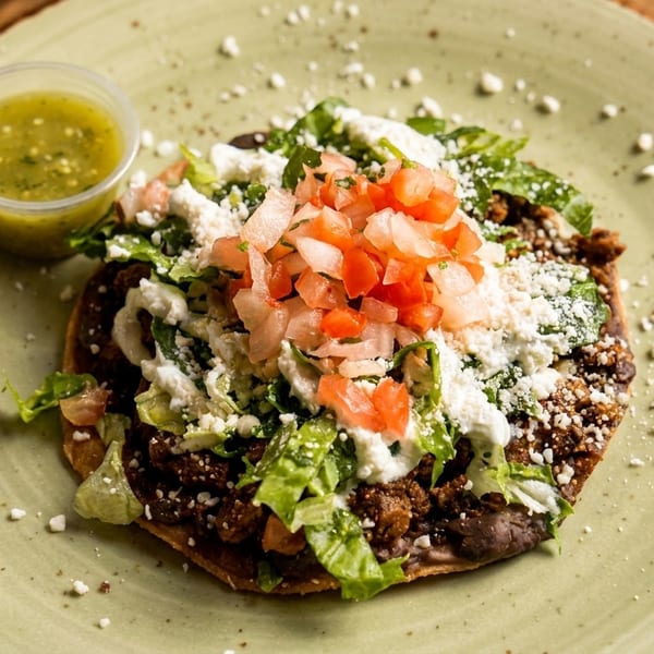 A tostada with meat, lettuce, cheese, and pico de gallo, served with green salsa.