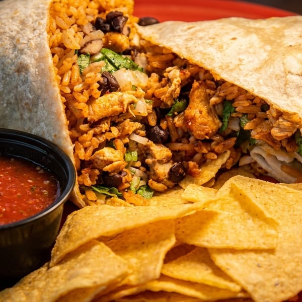 A large, cut burrito filled with rice, beans, and chicken, served with salsa and tortilla chips.