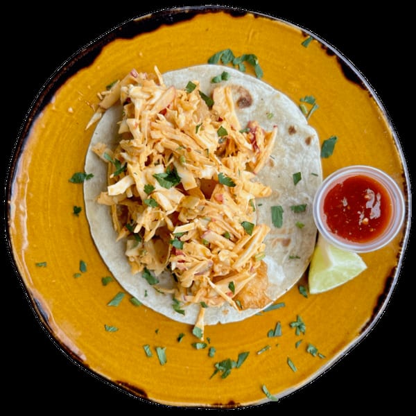 Top-down view of a fish taco with slaw and cilantro on a yellow plate with salsa and lime.