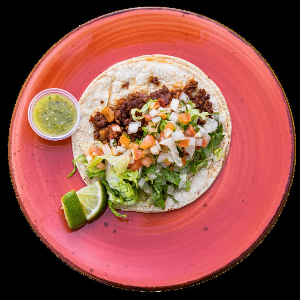 Overhead view of a taco with meat, lettuce, pico de gallo, lime, and green salsa on a red plate.